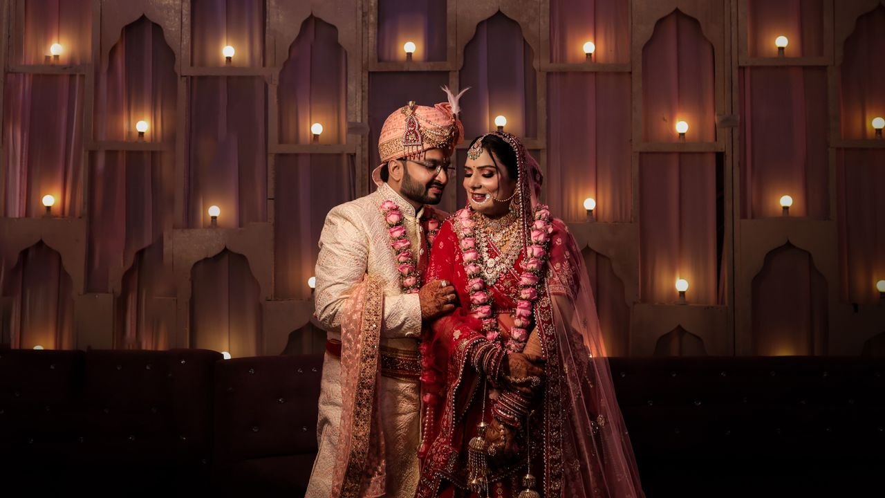 The Art of Drawing Readers In: Your attractive post title goes here Indian newlywed couple in traditional clothing, smiling and holding hands indoors.